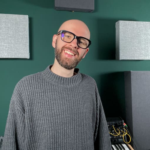 Ein Portrait von Maximilian Mumme in seinem Studio vor einer dunkelgrünen Wand mit Akustikelementen.